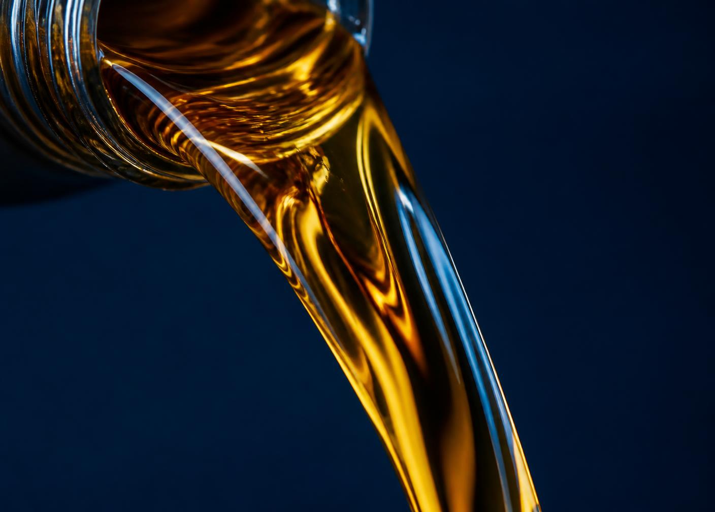 Golden lubricating oil pouring against a deep navy background